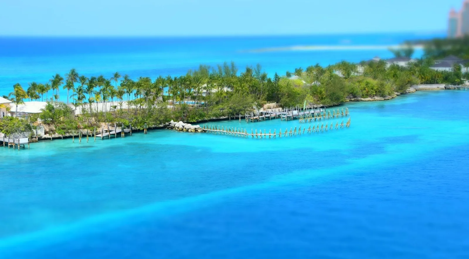 Aerial view of a palm-lined cay and timber dock pilings in turquoise water near Nassau