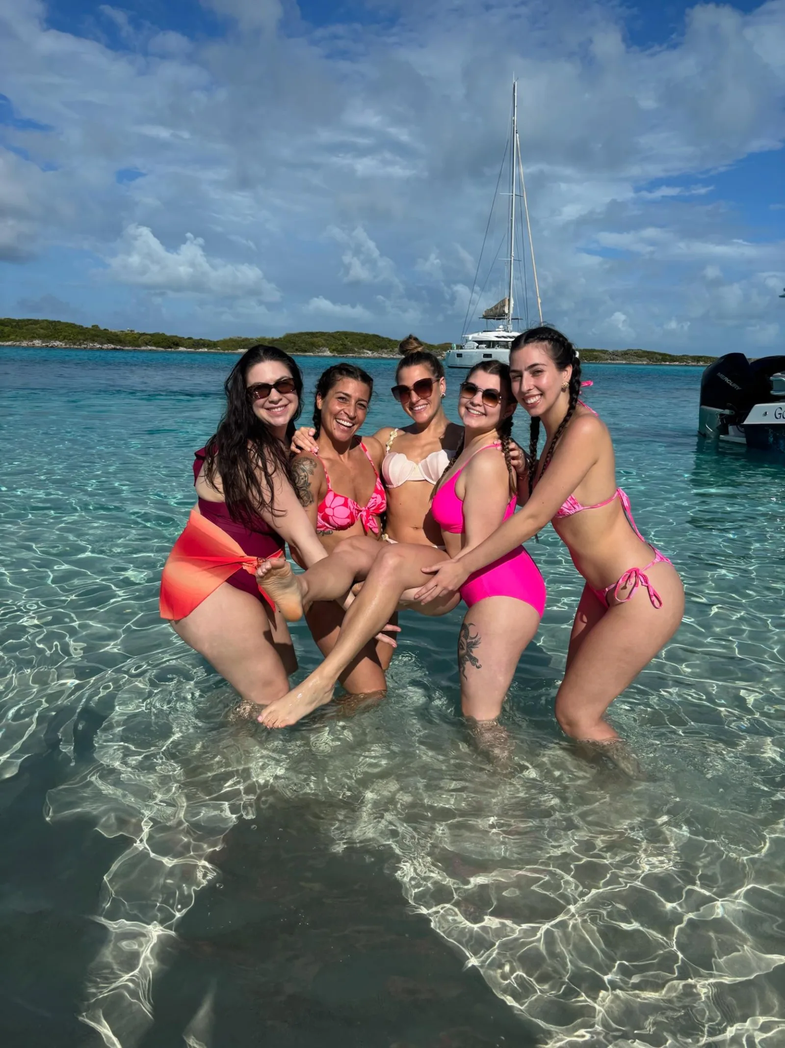 Four visitors sitting on the sandbar in bright shallows with the powerboat behind them