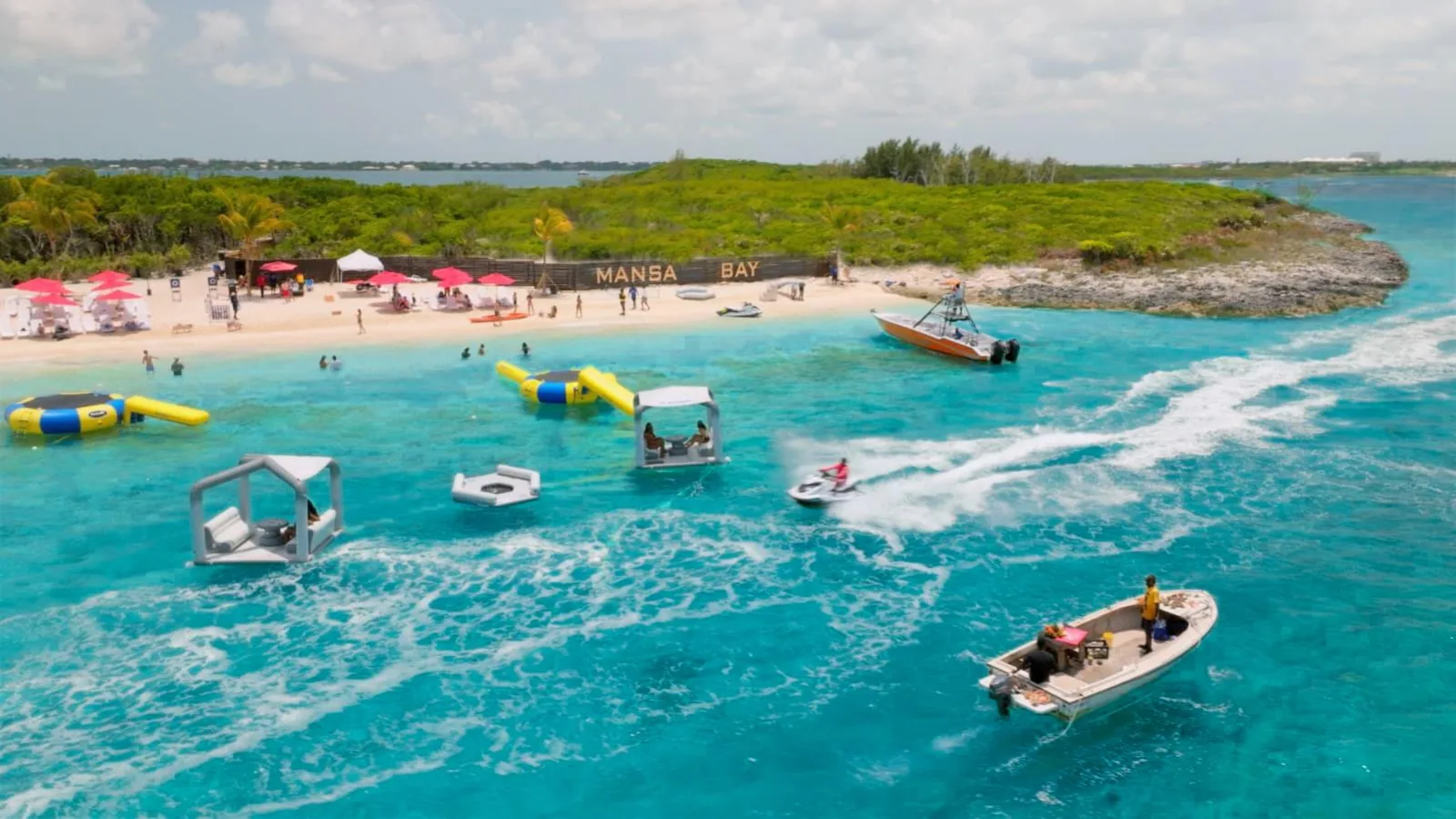 The island beach seen from the water, with floats, boats and visitors along the shore