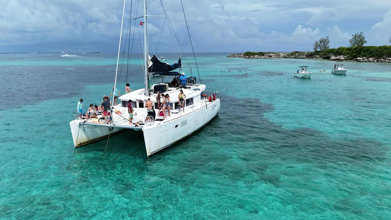 A white catamaran anchored in shallow turquoise water off a low green cay near Nassau