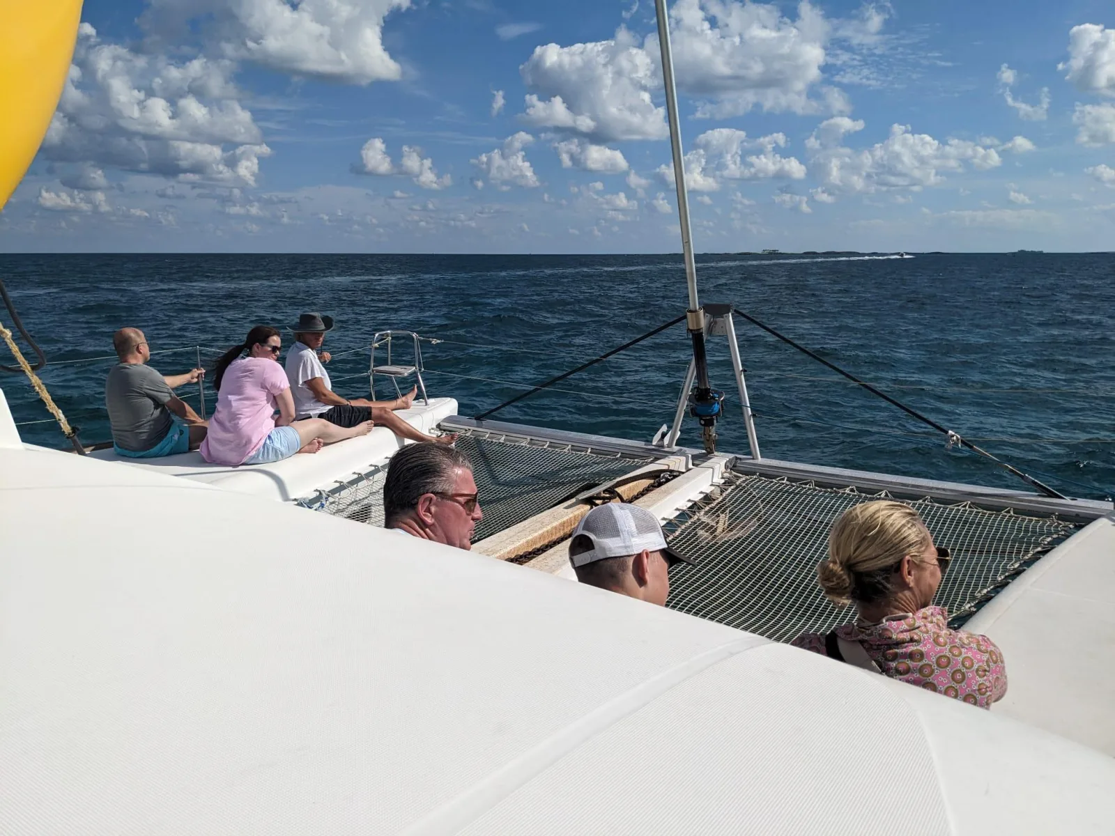 Passengers sitting along the rail of the catamaran under sail on a bright day