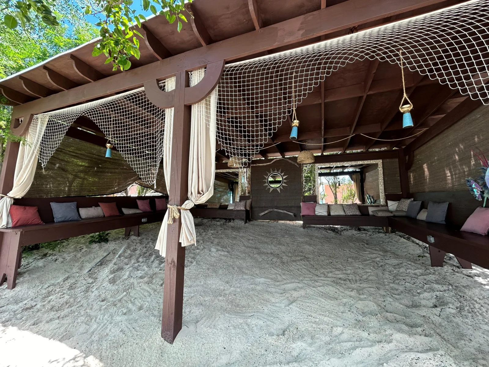 A shaded cabana with hanging nets and loungers at the private beach club