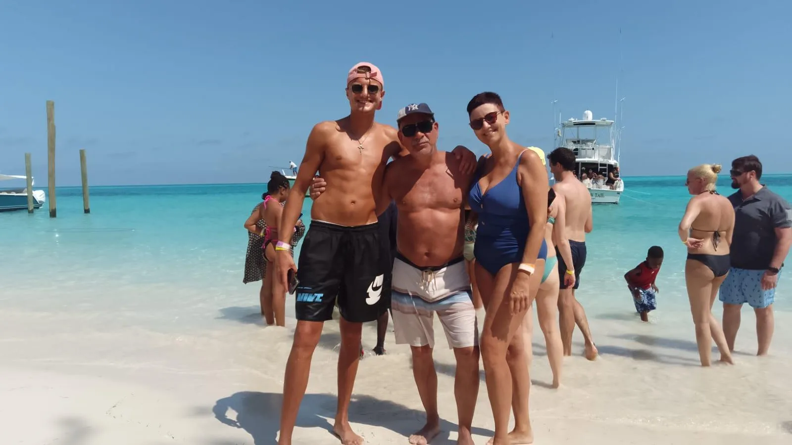 The charter group standing together on the beach beside a pig and a moored boat